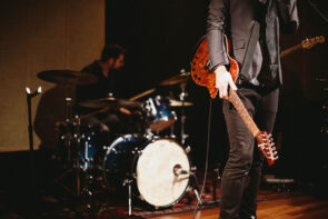 Musician holding guitar with drummer in background