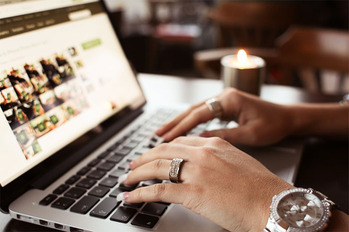 Hands wearing rings typing on laptop near candle