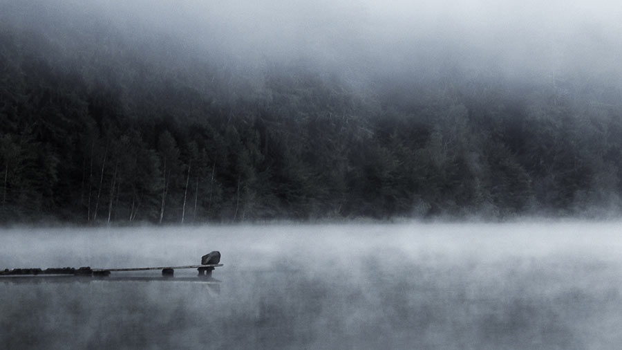 Solitary figure sitting on misty lakeside dock
