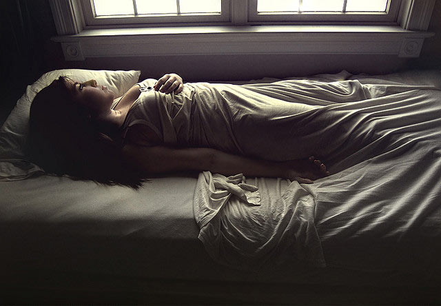 Woman lying on bed beside window