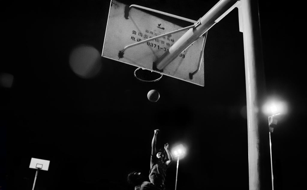 Nighttime basketball player reaching for hoop