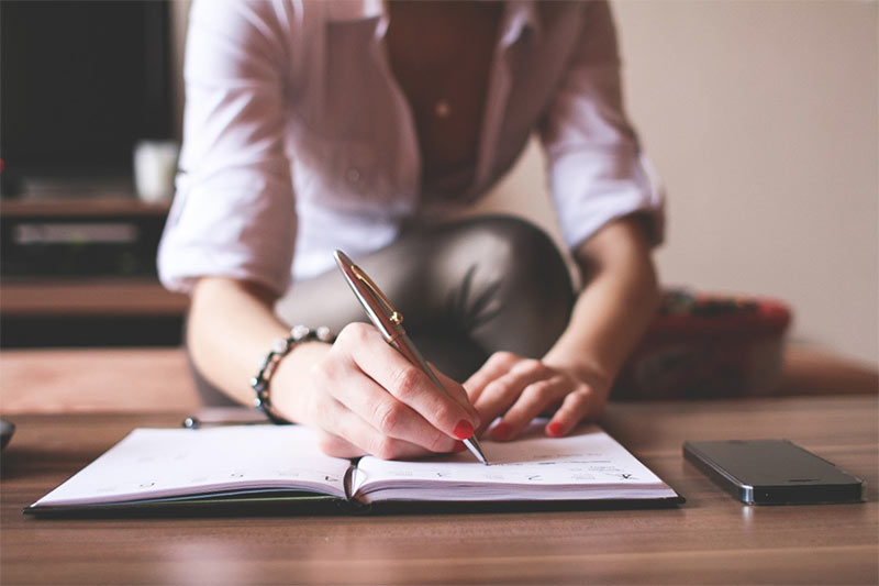Person writing in notebook with smartphone nearby