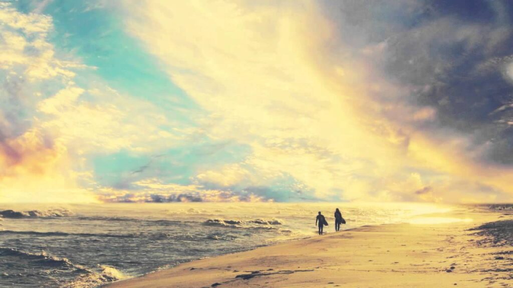 Two silhouettes walking on beach under dramatic sky