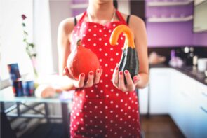 Person in kitchen apron holding two decorative gourds